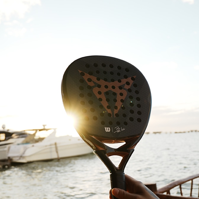 A technician in a grey jumpsuit inspecting the engine bay of a CUPRA Terramar in a studio; the background features a large screen displaying a close-up of metallic gears.