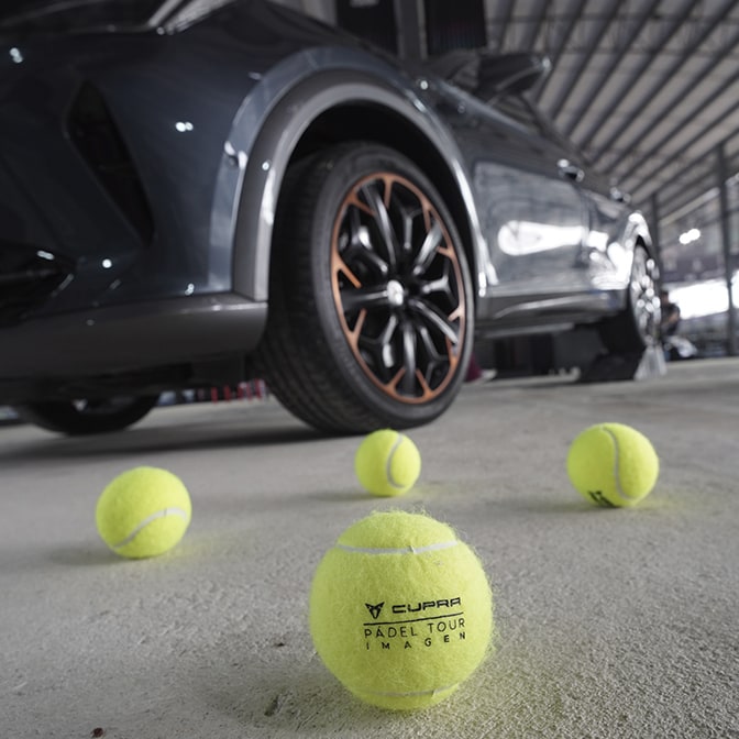 A technician in a grey jumpsuit inspecting the engine bay of a CUPRA Terramar in a studio; the background features a large screen displaying a close-up of metallic gears.